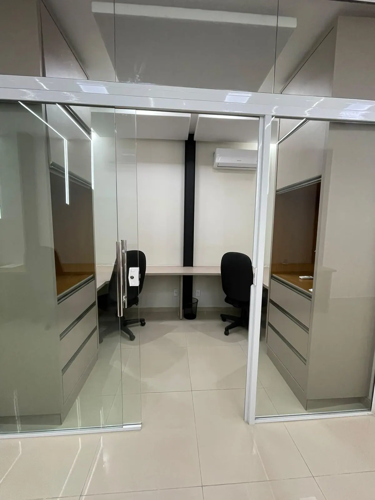 Sala privativa com porta de vidro, duas mesas, cadeiras e armários