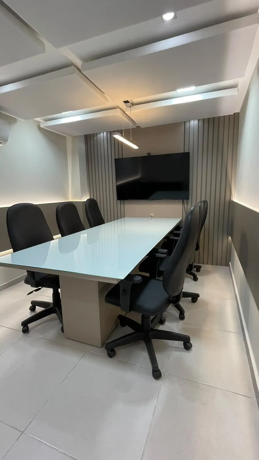 Sala de reunião em outro ângulo, com iluminação indireta e painéis acústicos no teto